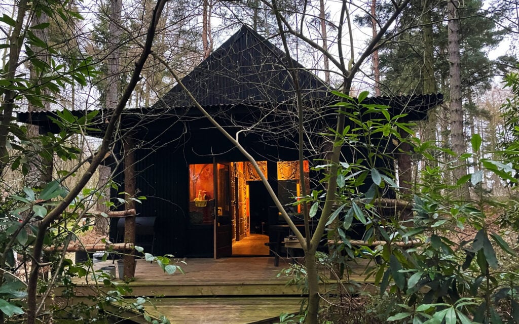 Woodland bothy glowing at dusk among the trees at The Dreamery Hideaway