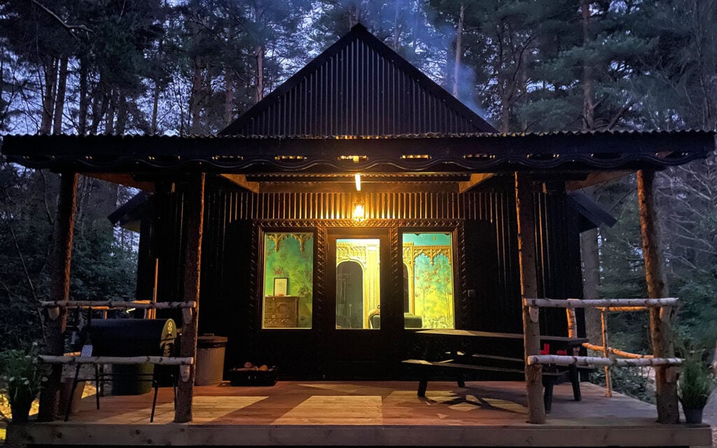 Woodland bothy at night lit warmly among trees