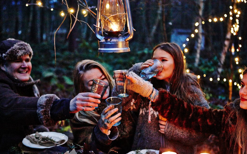 Guests sharing drinks beneath lanterns in a woodland setting
