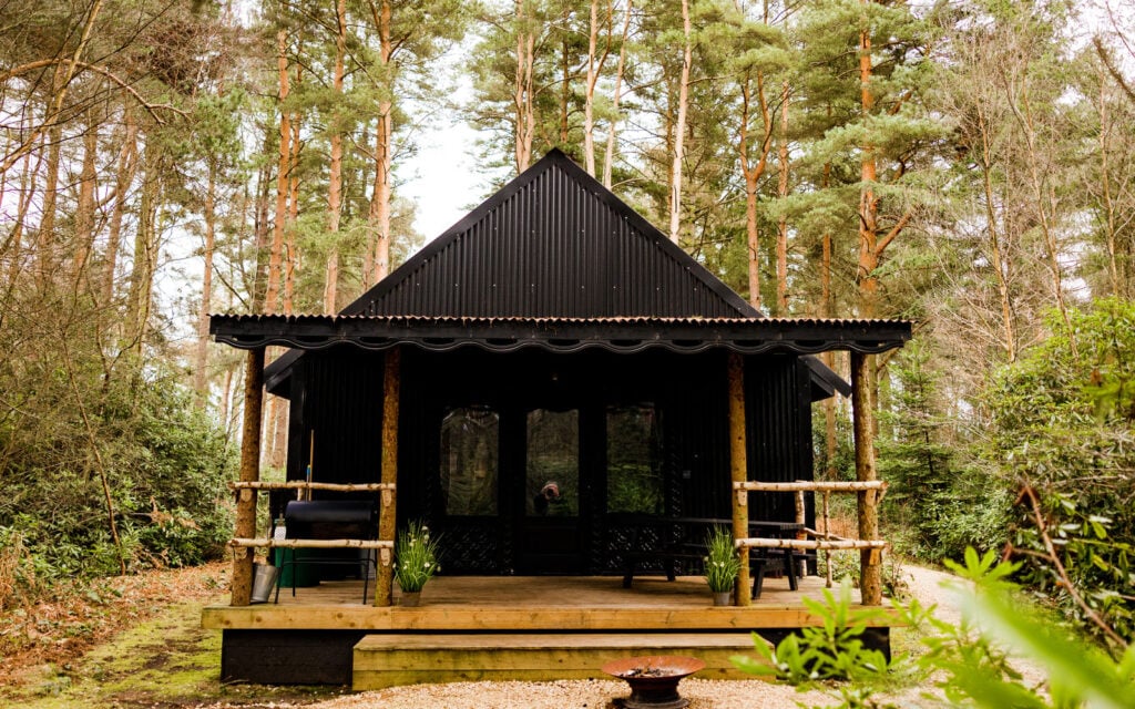 Exterior of a black woodland bothy at Dreamery Hideaway surrounded by trees