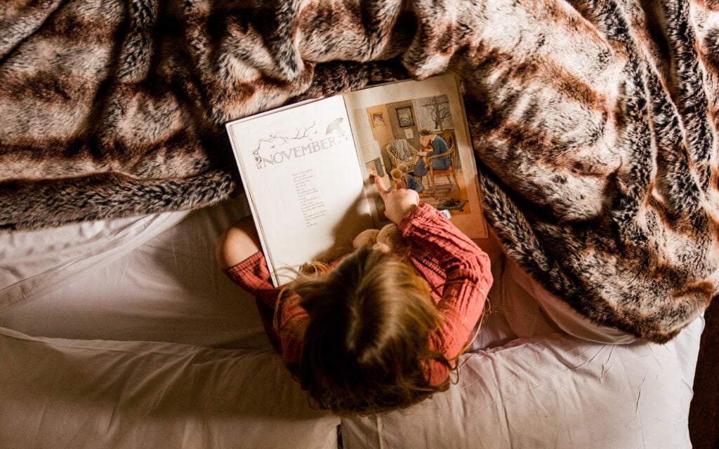 Child reading a storybook on a cosy bed at The Dreamery Hideaway